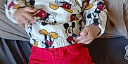 Issiaga participe au concours pour gagner de l'argent avec cette photo : baby, child, mickey_mouse, sweater, red_pants, brown_shoes, cushion, pillow, woven_backdrop, indoor, portrait, person, cute, infant, clothing, fashion, hand, face, expression, relaxing