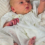 Rose is registered to the contest to win money with this photo: baby, infant, newborn, white_gown, polka_dots, blanket, soft_texture, cute, portrait, skin, hand, foot, sleepy, closeup, child, young, resting, cozy, indoors, expression