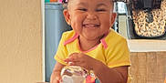 Dakota is registered to the contest to win money with this photo: toddler, smiling, child, bottle, socks, yellow_clothing, hair_buns, indoor, couch, happy, person, baby, home, furniture, high_chair, sitting, cute, playful, portrait, infant