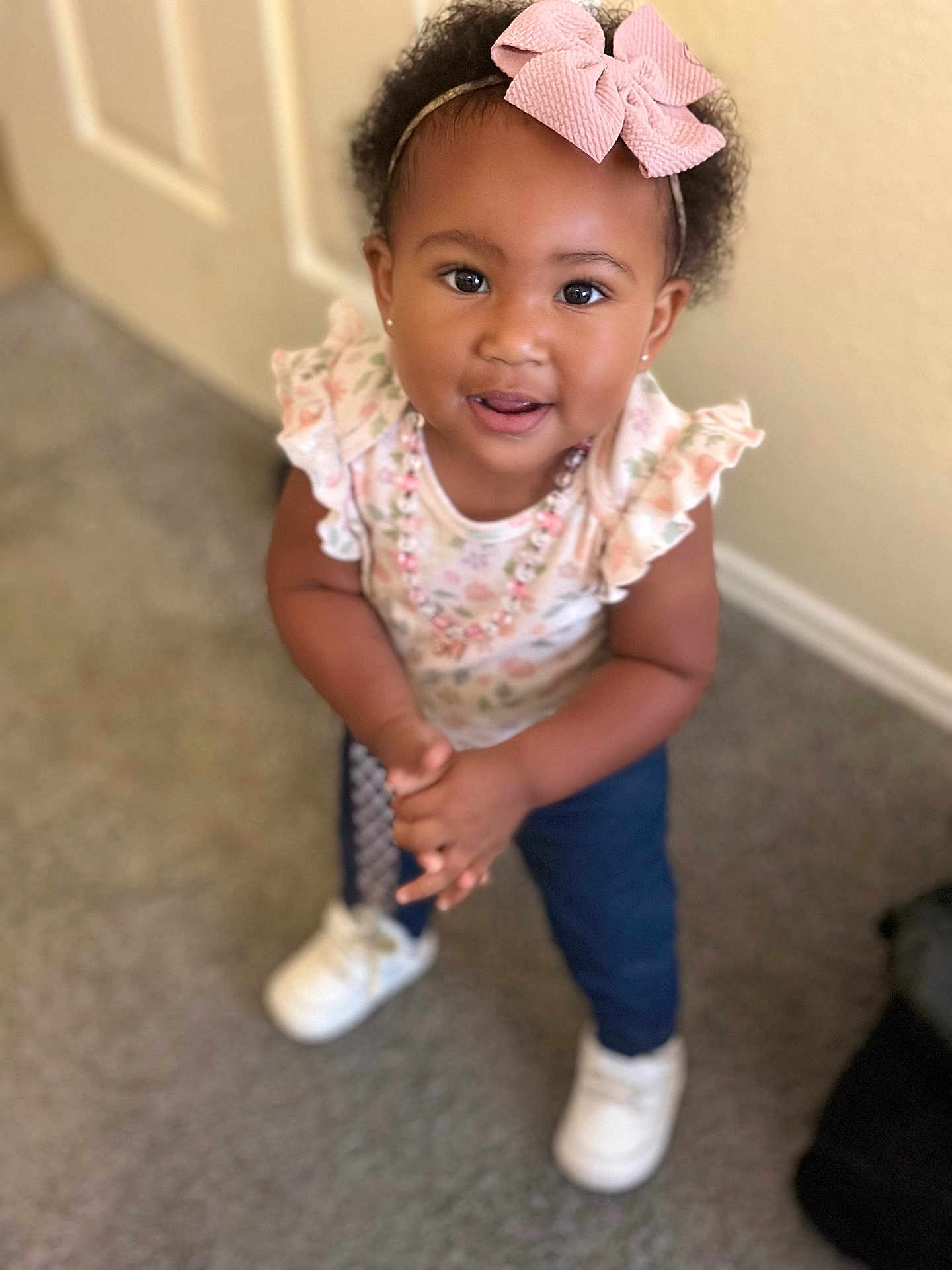 Dakota joined the competition — help win amazing prizes! toddler, child, girl, bow, hair, curly_hair, smile, standing, white_shoes, floral_top, navy_pants, carpet, indoor, cute, jewelry, earrings, happy, portrait, person, fashion