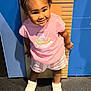 Dakota is registered to the contest to win money with this photo: toddler, child, yellow_bow, pink_shirt, striped_shorts, white_shoes, height_chart, smiling, standing, indoors, measurement, cute, happy, person, headband, floor, playful, young_child, portrait, clothing