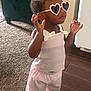 accessory, carpet, child, clothing, confident, cute, fashion, footwear, girl, hair_bow, heart_shaped, indoor, person, pink_pants, standing, sunglasses, toddler, white_top, wooden_floor, young_child