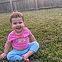 child, toddler, baby, smiling, laughing, grass, backyard, wooden_fence, pink_shirt, blue_pants, barefoot, sitting, portrait, outdoors, sunlight, happy, short_hair, earrings, playtime, casual_clothing