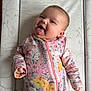baby, infant, child, smiling, tongue_out, floral_clothing, onesie, lying_down, changing_pad, patterned_background, animal_drawings, cheeky, cute, happy, pink, yellow, purple, hands, face, head