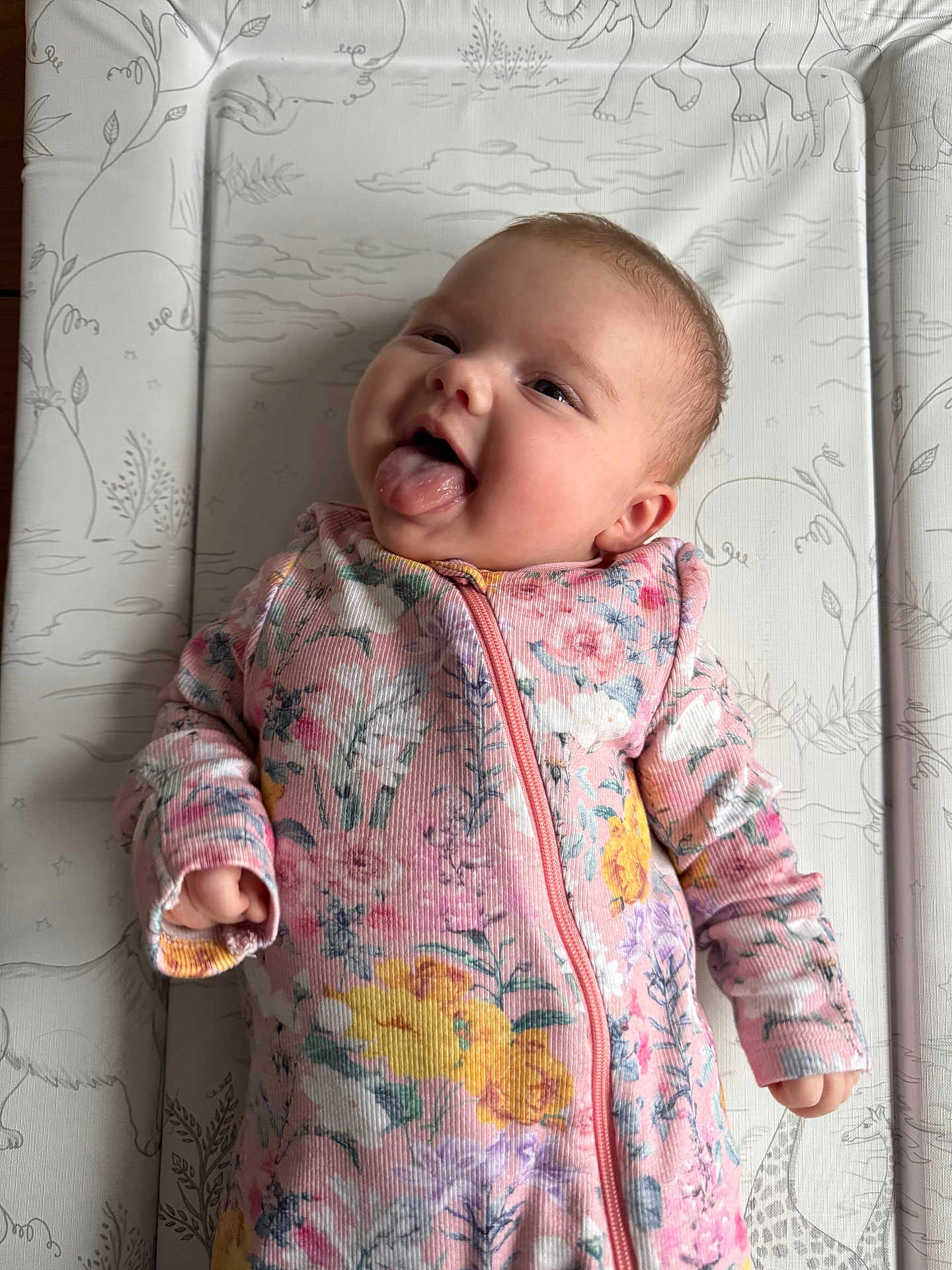 Rosa joined the competition — help win amazing prizes! baby, infant, child, smiling, tongue_out, floral_clothing, onesie, lying_down, changing_pad, patterned_background, animal_drawings, cheeky, cute, happy, pink, yellow, purple, hands, face, head