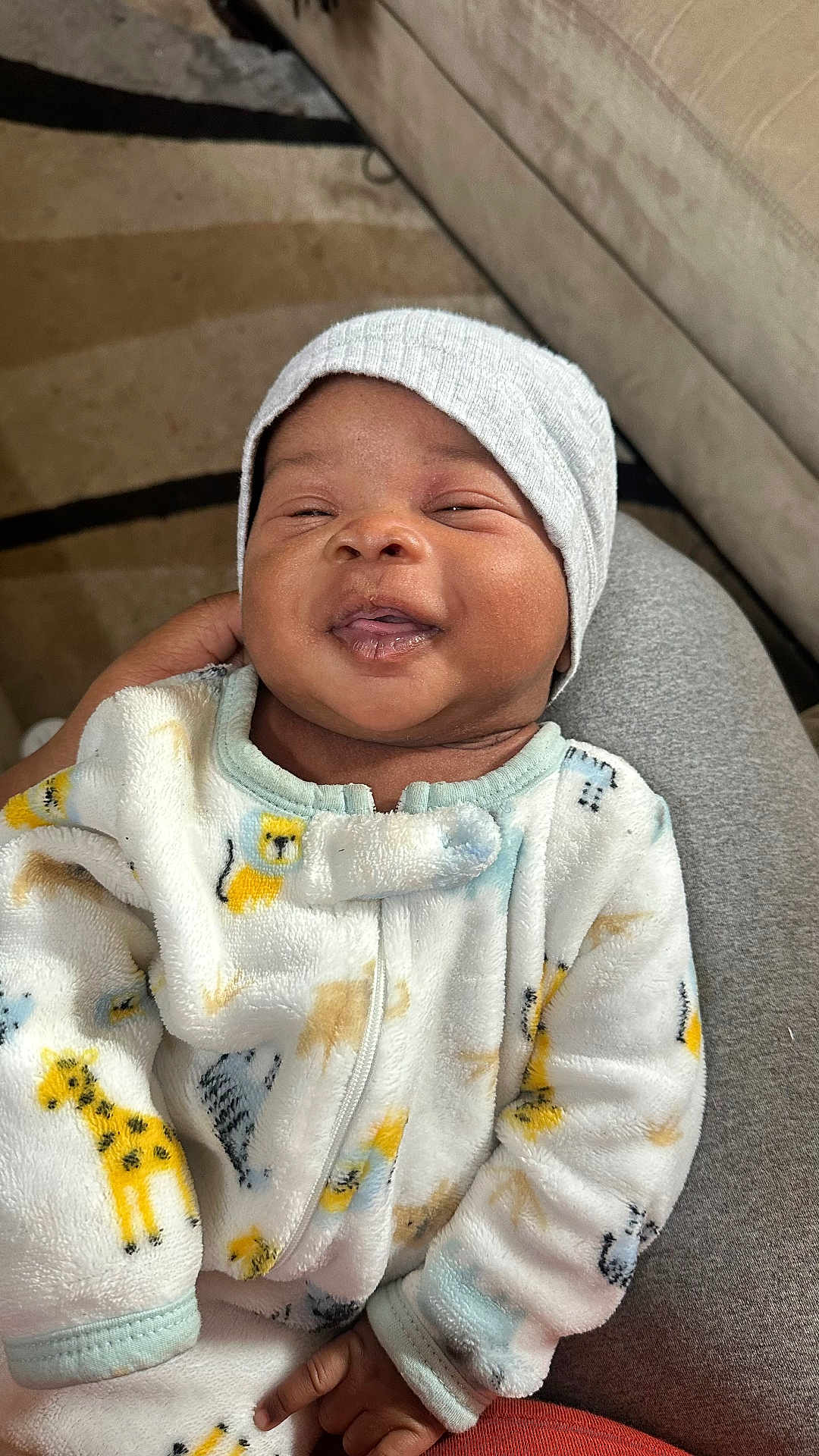 Sire joined the competition — help win amazing prizes! baby, infant, smiling, face, onesie, animal_print, hat, beanie, hand, lap, person, indoor, couch, fabric, cozy, cute, child, happy, portrait, soft