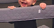 Mason is registered to the contest to win money with this photo: baby, child, playpen, smiling, happy, indoor, toy, soft_toy, clothing, pants, black_shirt, mesh, hands, face, head, infant, cute, standing, home, baby_toy