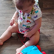 Willow is registered to the contest to win money with this photo: toddler, child, toy, floor, indoor, pull_toy, colorful, curious, sitting, clothing, hair, person, play, wood_floor, red, blue, white, pattern, butterfly, casual