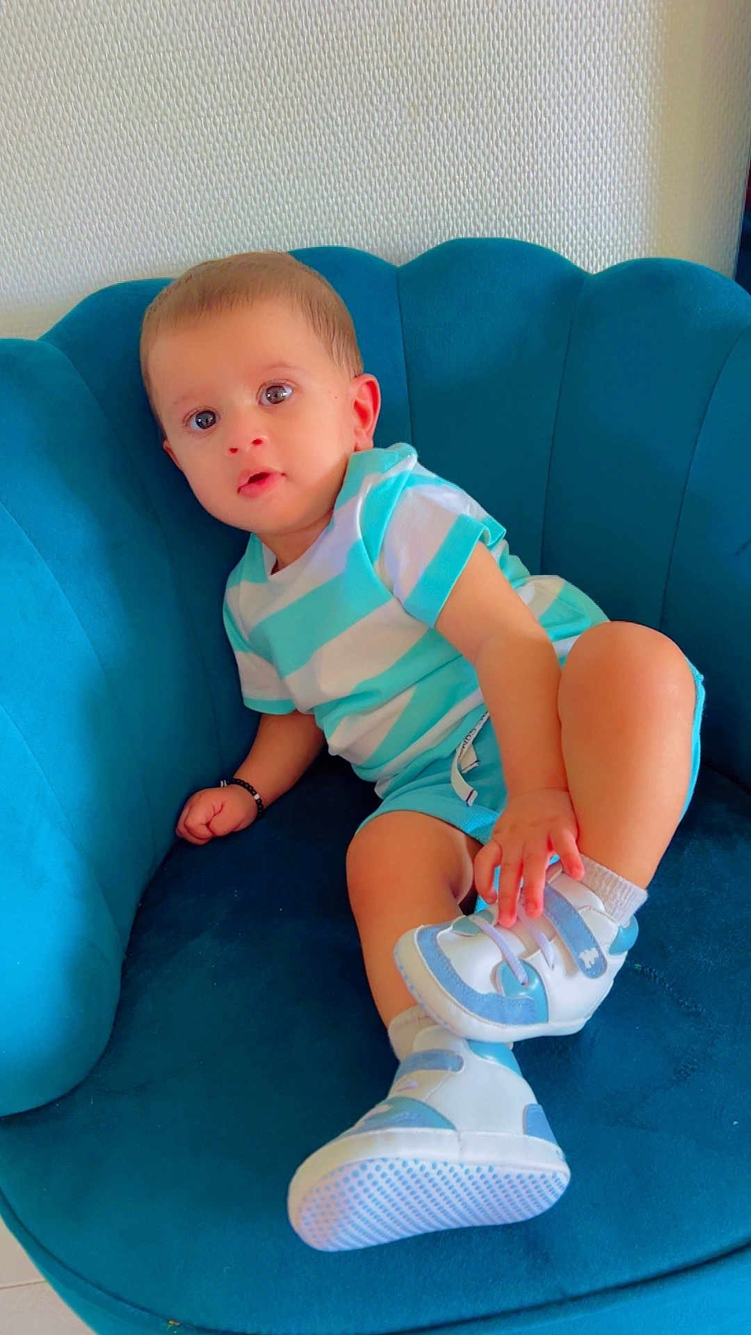 Adam participe au concours pour gagner de l'argent avec cette photo : toddler, child, blue_chair, striped_shirt, shorts, sneakers, white_socks, indoor, portrait, curious, cute, comfortable, plush, seated, young_child, baby, casual_clothing, small_hand, expression, relaxed