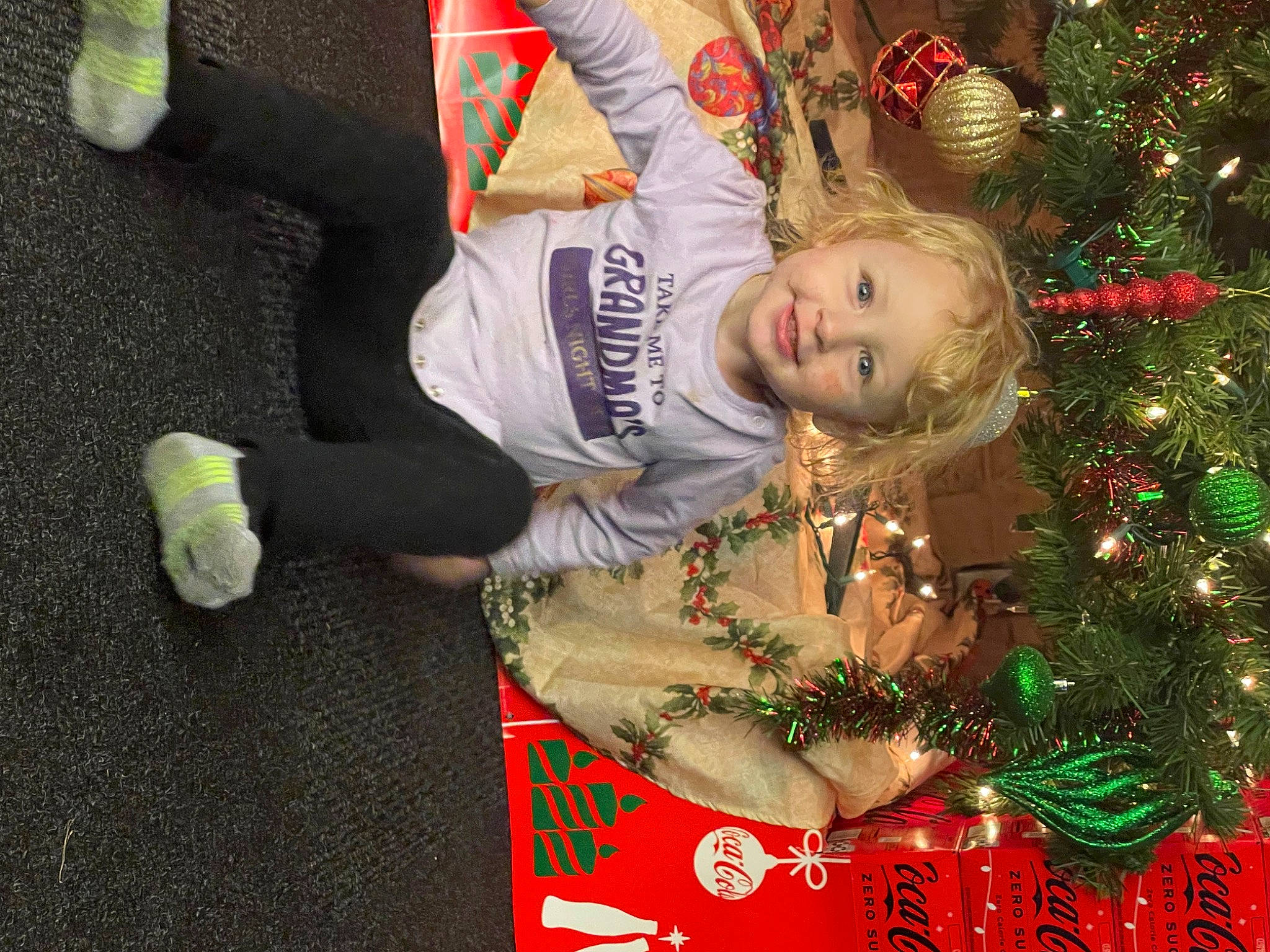 Mallie is registered to the contest to win money with this photo: baby_toddler_clothing, christmas, christmas_decoration, christmas_eve, christmas_ornament, christmas_tree, conifer, event, green, happy, holiday, holiday_ornament, human_body, joy, lap, mammal, ornament, person, plant, toddler