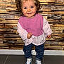 toddler, child, smiling, curly_hair, blue_bow, pink_vest, blouse, jeans, heart_patches, sneakers, standing, indoor, wooden_wall, floor_tiles, happy, portrait, young_child, fashion, cute, person