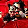Maylone a rejoint le concours — aidez-le/la à gagner de superbes lots ! baby, child, mickey_mouse, hat, red_couch, plush_toy, pacifier, smiling, crawling, black_shirt, toy, decor, balloon, indoor, person, cute, happy, soft_toy, celebration, bright