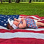 american_flag, baby, barefoot, checkered_pattern, child, dress, grass, greenery, head, headband, infant, lying_down, nature, outdoor, patriotic, peaceful, resting, side_view, skin, summer