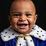 baby, child, smiling, crown, cape, royalty, blue, fur_trim, portrait, happy, face, headwear, costume, cute, infant, black_background, clothing, jewels, celebration, studio