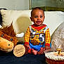 baby, child, cowboy_costume, plush_toy, stuffed_animal, couch, pillow, cake, birthday_candle, celebration, milestone, smiling, indoors, happy, sitting, face, foot, hand, wooden_sign, number_seven