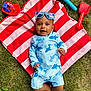 baby, child, grass, towel, striped_towel, sunglasses, blue_sunglasses, swimsuit, shark_print, beach_toys, red_shovel, blue_rake, red_toy_boat, outdoor, summer, happy, smiling, barefoot, playing, lying_down