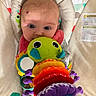 baby, baby_seat, caterpillar, child, closeup, clothing, colorful, comfort, cute, fabric, face, head, indoor, infant, looking, patterned, pink_bib, playtime, soft_toy, toy