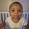 Jacob is registered to the contest to win money with this photo: toddler, child, crib, onesie, cartoon, lion, baby, indoor, nursery, grip, smile, cute, face, person, infant, expression, clothing, furniture, young_child, standing