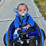 baby, child, pacifier, toy_car, blue_jacket, sidewalk, grass, outdoor, sunlight, shadow, parking, car, holding, steering_wheel, cute, young_child, seatbelt, play, person, vehicle
