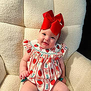 Presley is registered to the contest to win money with this photo: baby, child, red_bow, strawberry_pattern, cute, smiling, sitting, cream_chair, soft_texture, indoors, happy, infant, cute_outfit, headwear, plush_chair, adorable, portrait, person, young_child, cozy