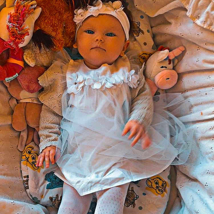 Rose-Shanna a rejoint le concours — aidez-le/la à gagner de superbes lots ! baby, bed, blanket, calm_expression, child, cute, doll, headband, indoor, infant, lying_down, patterned_blanket, plush_toys, portrait, sleepwear, soft_lighting, tights, toy, unicorn, white_dress