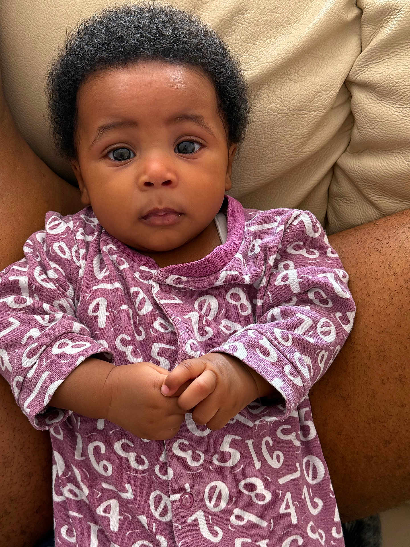 Eliora joined the competition — help win amazing prizes! baby, child, infant, portrait, clothing, purple, numbers, onesie, hands, face, eyes, curly_hair, couch, leather, skin, sitting, indoor, person, cute, expression