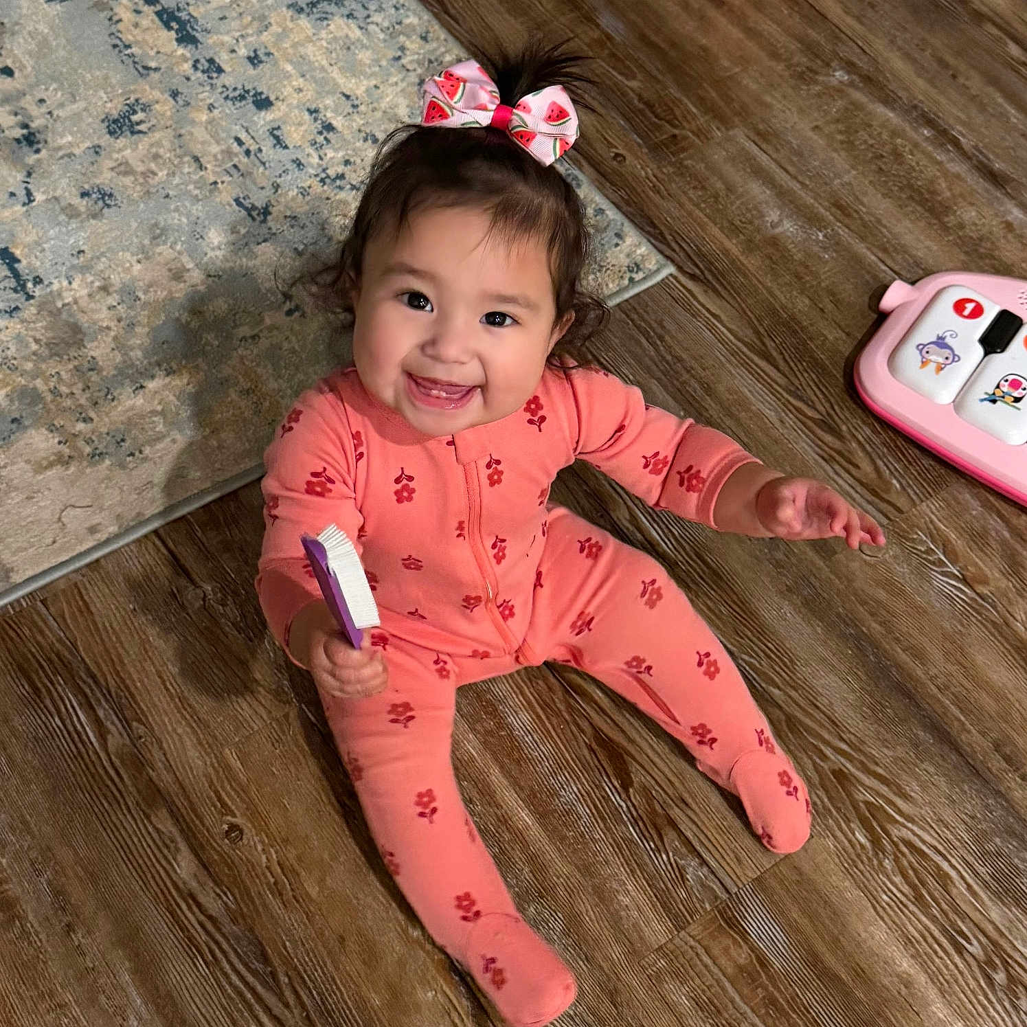 Leiana is registered to the contest to win money with this photo: baby, brush, child, cute, eyes, face, hair_bow, happy, home, indoor, pajamas, pink, playtime, rug, sitting, smiling, teeth, toddler, toy, wooden_floor