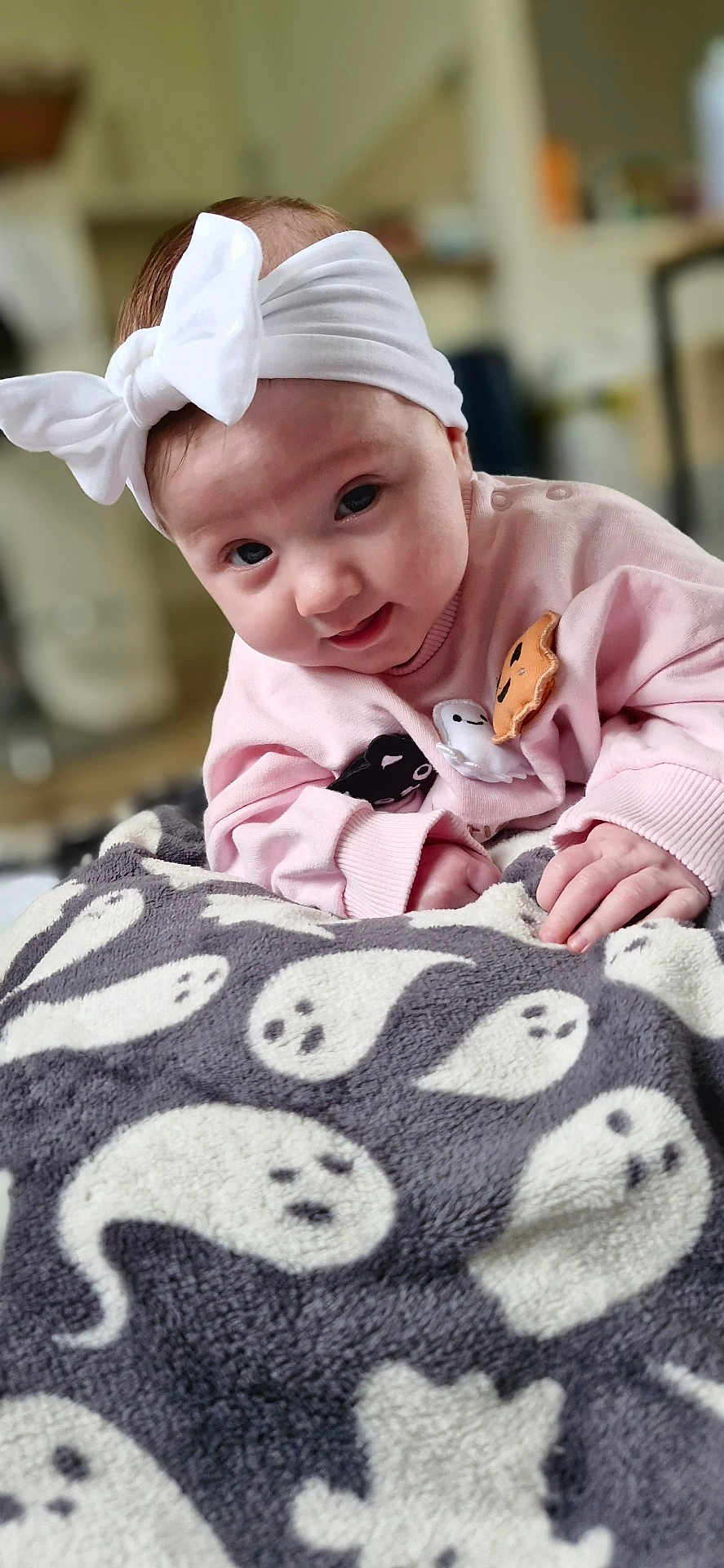 Nora is registered to the contest to win money with this photo: baby, infant, headband, bow, pink_sweater, blanket, ghost_pattern, smile, cute, face, hand, cozy, indoors, child, soft_texture, portrait, young, adorable, warm, clothing