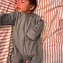 baby, sleeping, onesie, bed, pillow, striped_sheets, infant, cozy, peaceful, child, soft_fabric, rest, cute, indoors, young_child, comfort, nap, portrait, person, sleepwear