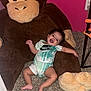 baby, smiling, plush_toy, giant_monkey, carpet, pink_wall, onesie, happy, indoor, child, toy, cute, person, infant, playful, room, floor, toddler, clothing, furniture