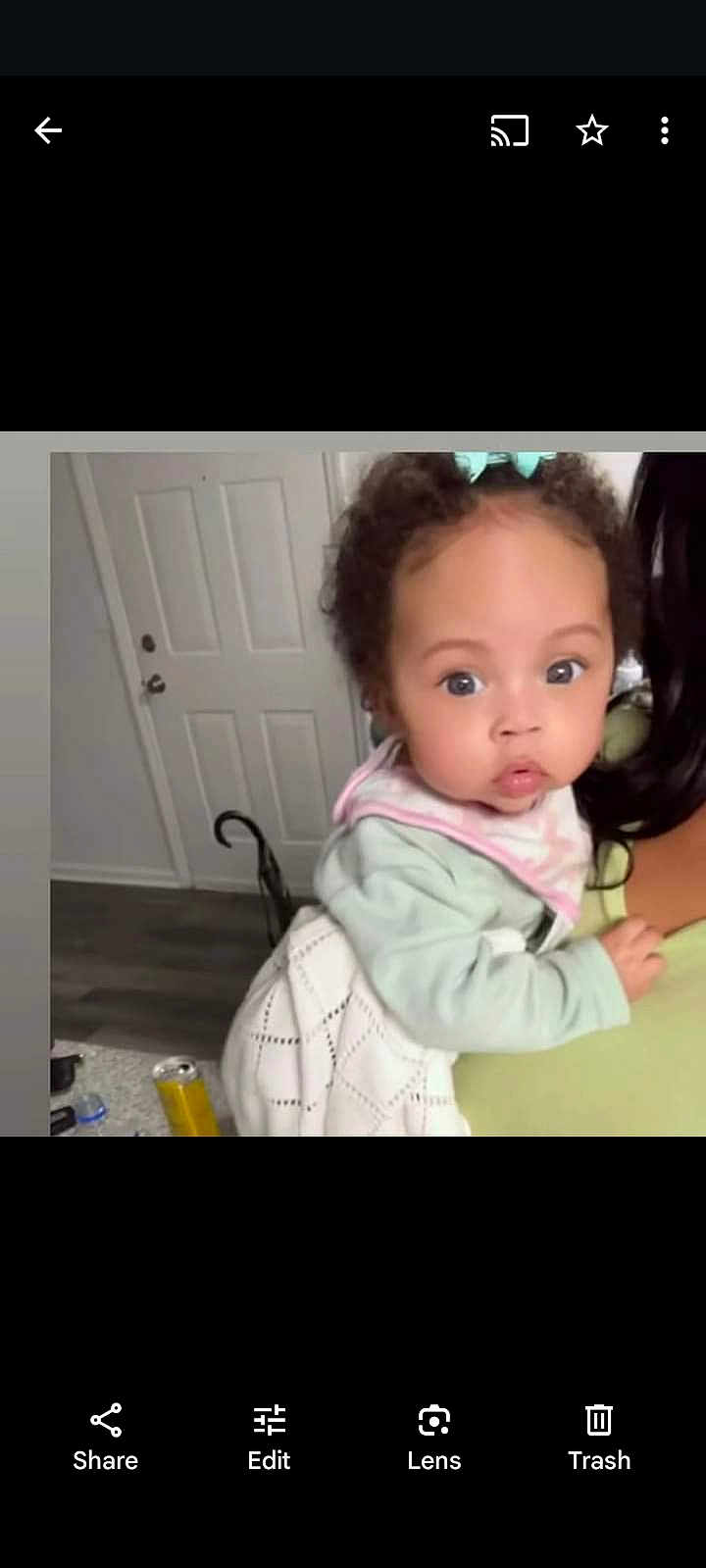 Sienna Leigh is registered to the contest to win money with this photo: baby, child, indoor, person, curly_hair, bib, light_clothing, holding, door, floor, adult, face, eyes, expression, hand, hair_bow, home, furniture, curious, portrait