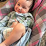 baby, infant, child, smiling, face, hair_spike, onesie, diaper, baby_bouncer, plaid_pattern, pink, gray, hand, carpet, fabric, seat, cozy, portrait, indoor, cute