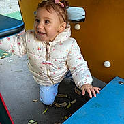 Aalyah a rejoint le concours — aidez-le/la à gagner de superbes lots ! toddler, child, playground, jacket, pink_bow, curly_hair, smile, outdoor, fall_leaves, play_structure, kneeling, blue_pants, happy, person, daylight, park, colorful, young_child, casual_clothing, cute
