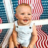 baby, child, smiling, happy, overalls, striped_clothing, sitting, face, blue_eyes, blond_hair, patterned_background, chair, american_flag_pattern, cute, innocence, portrait, skin, baby_skin, summer_clothes, young