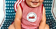 James is registered to the contest to win money with this photo: baby, child, smile, happy, red_hair, striped_clothing, sitting, barefoot, flag_pattern, american_flag, fire_truck, cute, portrait, indoors, infant, playful, bright, patterned_background, skin, face