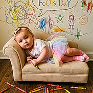 Samara is registered to the contest to win money with this photo: toddler, child, couch, crayons, colorful, scribbles, wall, wooden_floor, rainbow_skirt, headband, smiling, drawing, messy, indoor, playful, art, clothing, floor, portrait, happy