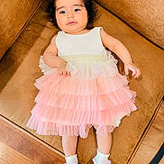 Aashna joined the competition — help win amazing prizes! baby, child, dress, pink, white, socks, flower, couch, brown, wooden_floor, indoor, curly_hair, cute, portrait, laying_down, infant, young_child, comfortable, soft_lighting, smiling_face
