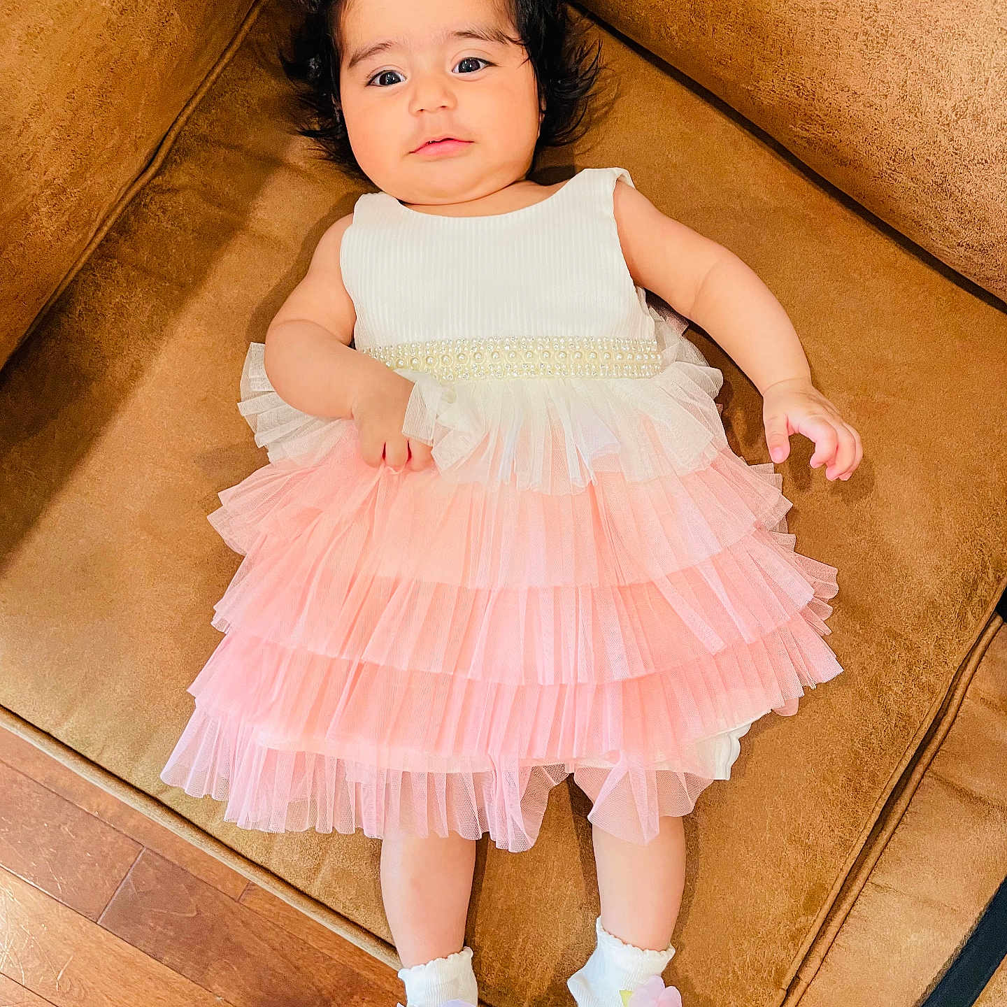 Aashna joined the competition — help win amazing prizes! baby, brown, child, comfortable, couch, curly_hair, cute, dress, flower, indoor, infant, laying_down, pink, portrait, smiling_face, socks, soft_lighting, white, wooden_floor, young_child