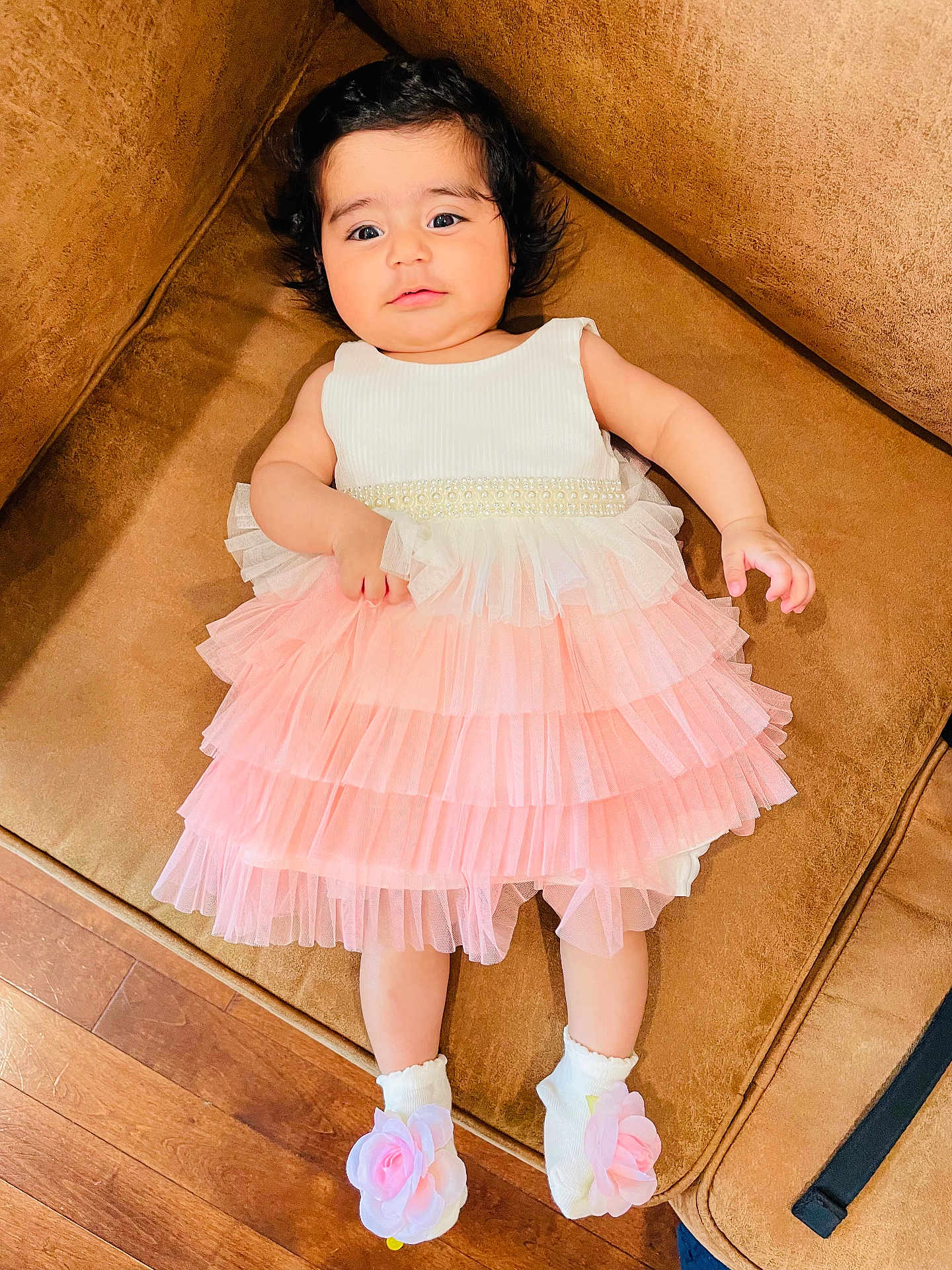 Aashna joined the competition — help win amazing prizes! baby, child, dress, pink, white, socks, flower, couch, brown, wooden_floor, indoor, curly_hair, cute, portrait, laying_down, infant, young_child, comfortable, soft_lighting, smiling_face