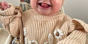 Indie joined the competition — help win amazing prizes! baby, child, high_chair, knitted_sweater, headband, bow, tongue_out, happy, smiling, indoors, cute, infant, person, face, hand, cozy, soft_lighting, close_up, seat, playful