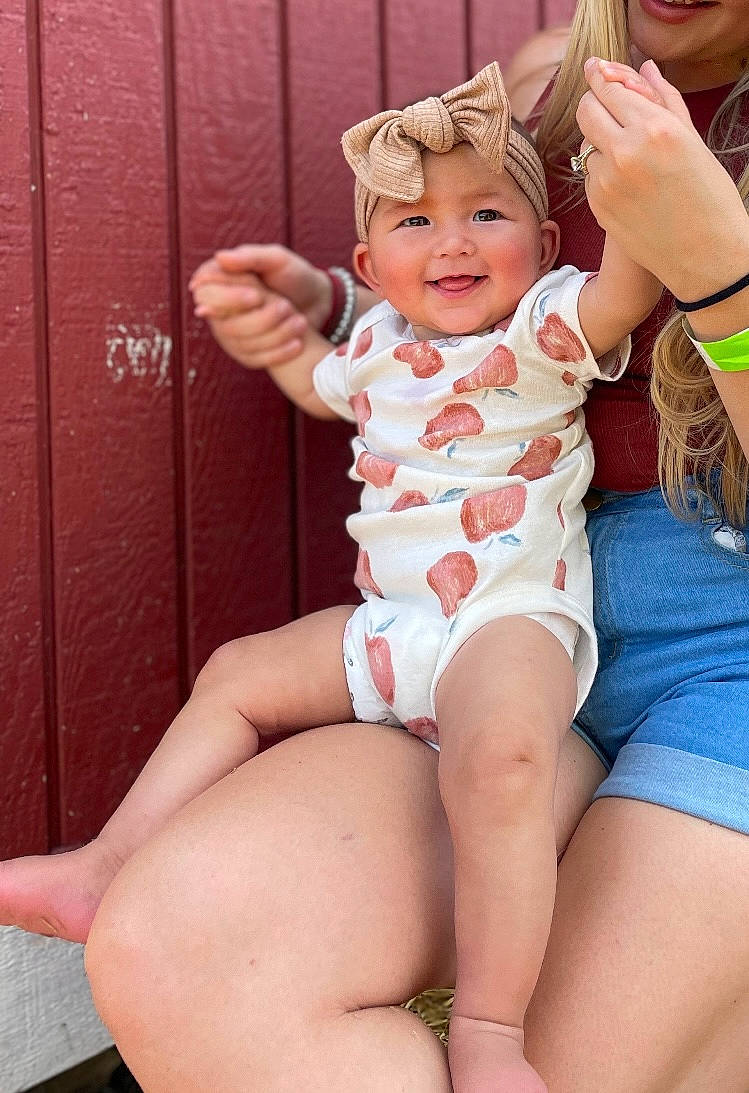 Harper is registered to the contest to win money with this photo: abdomen, arm, baby, baby_toddler_clothing, face, facial_expression, finger, gesture, hand, happy, headwear, joy, knee, leg, mouth, muscle, person, pink, skin, smile