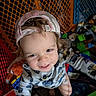 toddler, child, cap, smile, toy, playpen, indoor, clothing, happy, face, person, curly_hair, colorful, play_area, baby_toys, fence, cute, reaching, portrait, casual