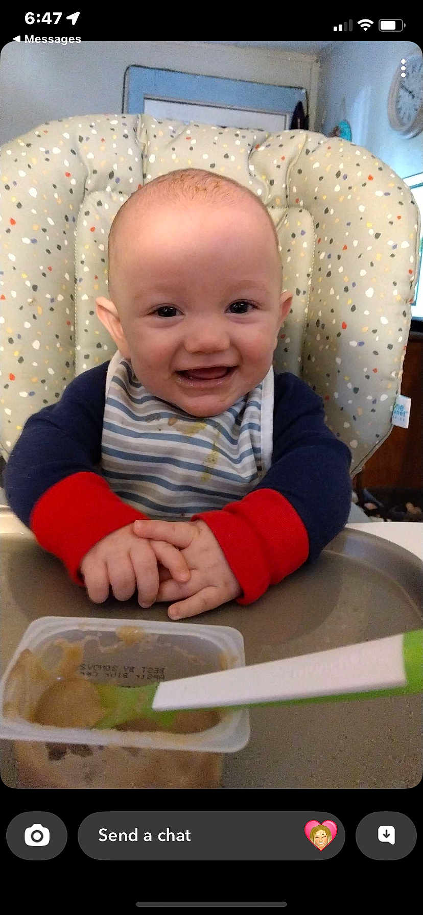 Atlus is registered to the contest to win money with this photo: baby, high_chair, bib, baby_food, spoon, smiling, happy, infant, feeding_time, cushion, striped_clothing, food_container, cute, indoors, child, person, face, hands, table, playful