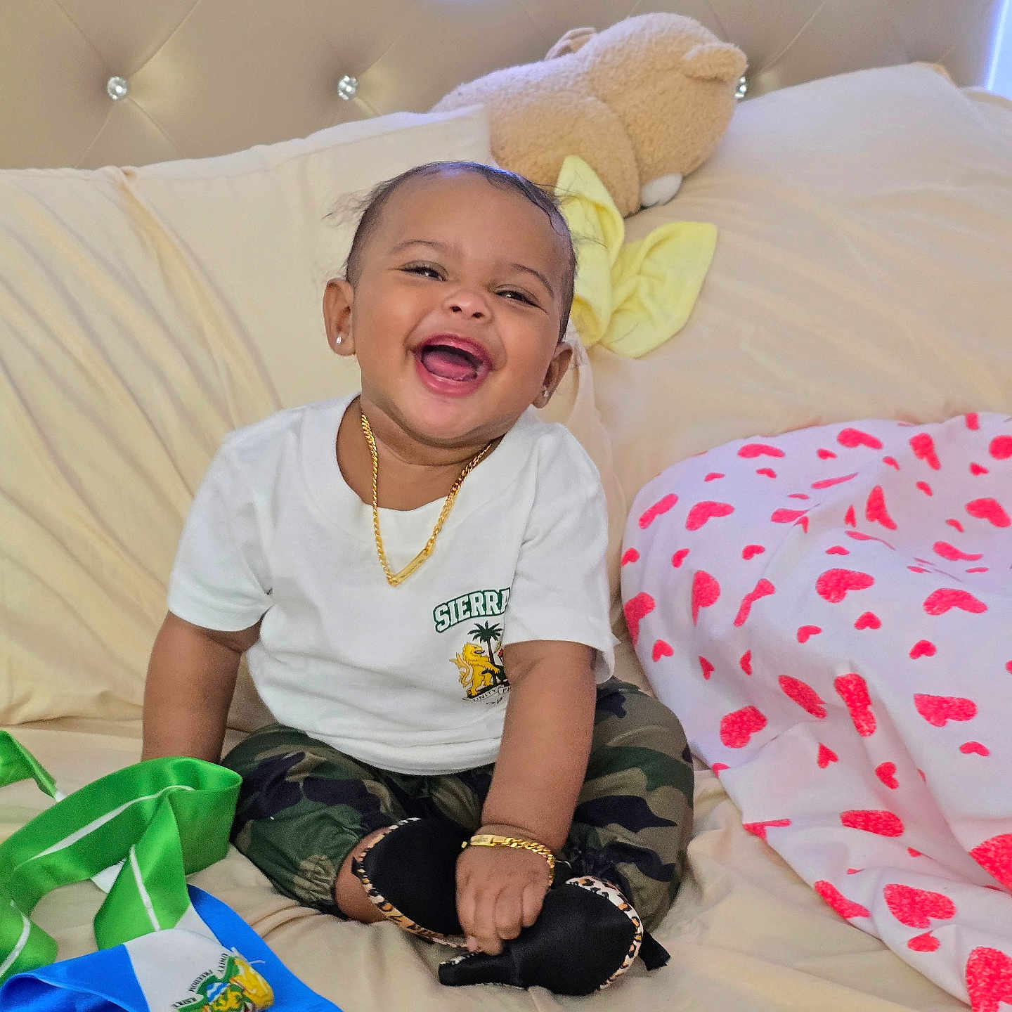Marjeta joined the competition — help win amazing prizes! baby, smiling, sitting, bed, teddy_bear, white_tshirt, camo_pants, black_shoes, gold_jewelry, ribbons, blanket, heart_pattern, happy, child, indoor, portrait, cute, accessory, soft_toy, comfortable