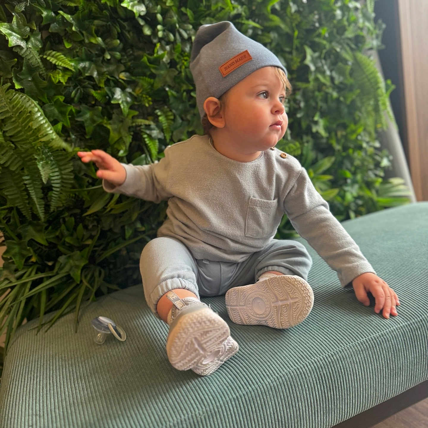 Ethyan joined the competition — help win amazing prizes! baby, beanie, bench, casual, child, cozy, curious, cute, face, greenery, grey_clothing, indoor, pacifier, plants, portrait, seated, sneakers, toddler, wooden_floor, young_child