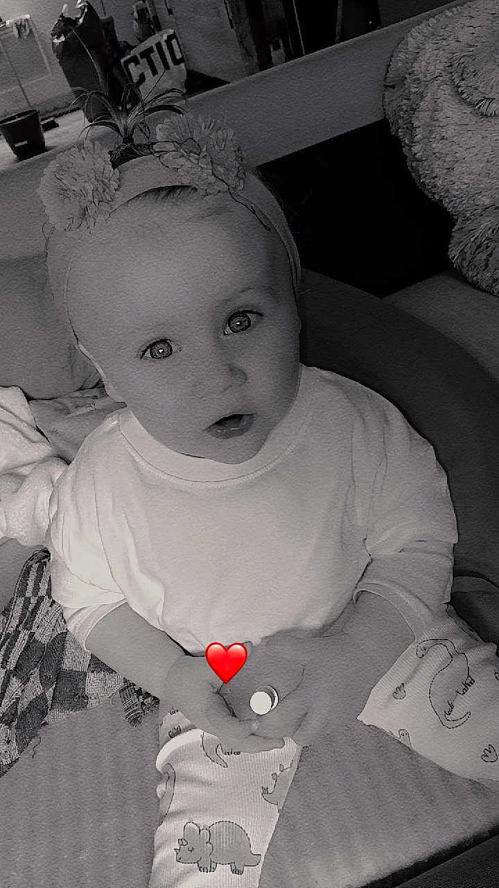 Aina participe au concours pour gagner de l'argent avec cette photo : baby, child, headband, pajamas, dinosaur_print, grayscale, indoors, sitting, cute, expression, face, hand, heart_emoji, blanket, cushion, soft_toys, clothing, person, infant, portrait