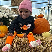 Cyleah Rogers is registered to the contest to win money with this photo: toddler, child, pumpkin, hay, orange_clothing, pink_beanie, socks, flowers, greenhouse, smiling, fall, harvest, cute, black_shirt, decor, seasonal, autumn, playful, festive, sitting