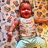 arm, baby, balloons, bluey_pattern, cartoon_print, chubby_cheeks, crib_sheet, dumbo_print, happy, infant, leg, lying_down, nursery_bedding, onesie, pastel_colors, playful, polka_dot_pants, portrait, smiling_baby, spiky_hair