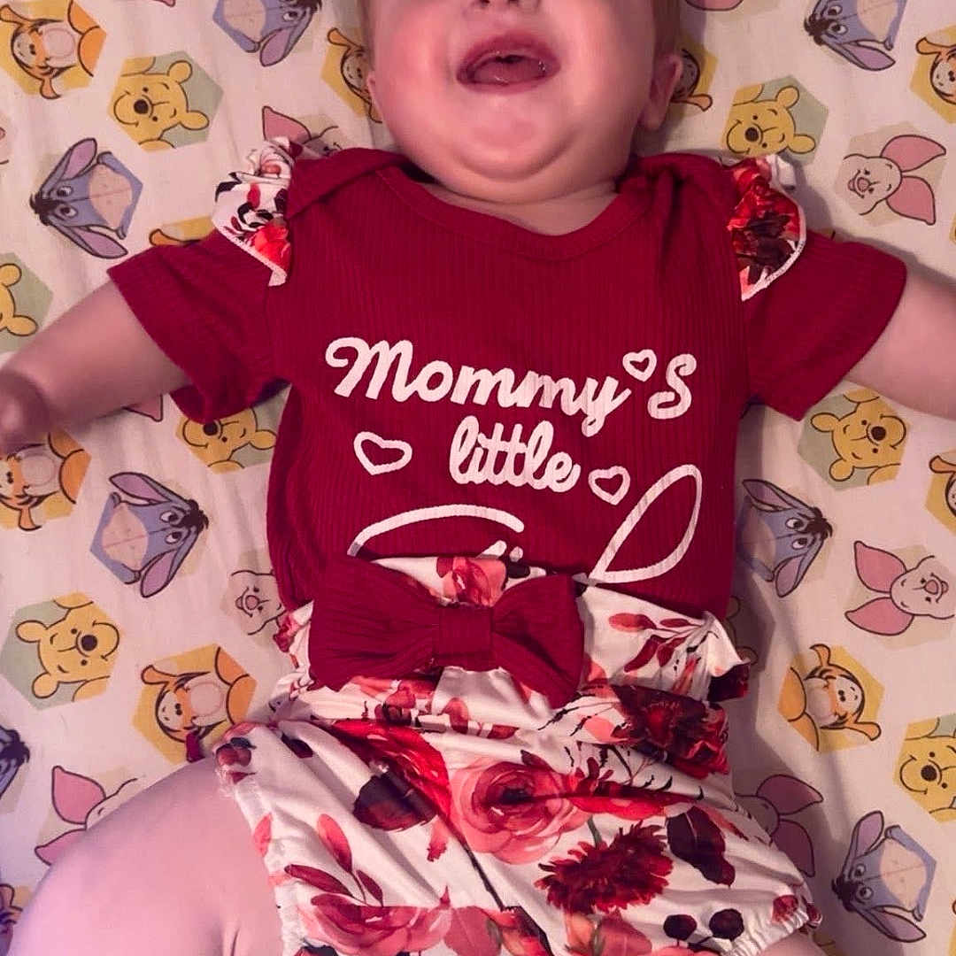 Shelbie joined the competition — help win amazing prizes! baby, bedroom, blanket, cartoon_pattern, child, cute, face, floral_romper, hair_tuft, happy, laughing, lying_down, onesie, pink_leggings, pooh_pattern, portrait, red_outfit, sheet, smiling, winnie_the_pooh