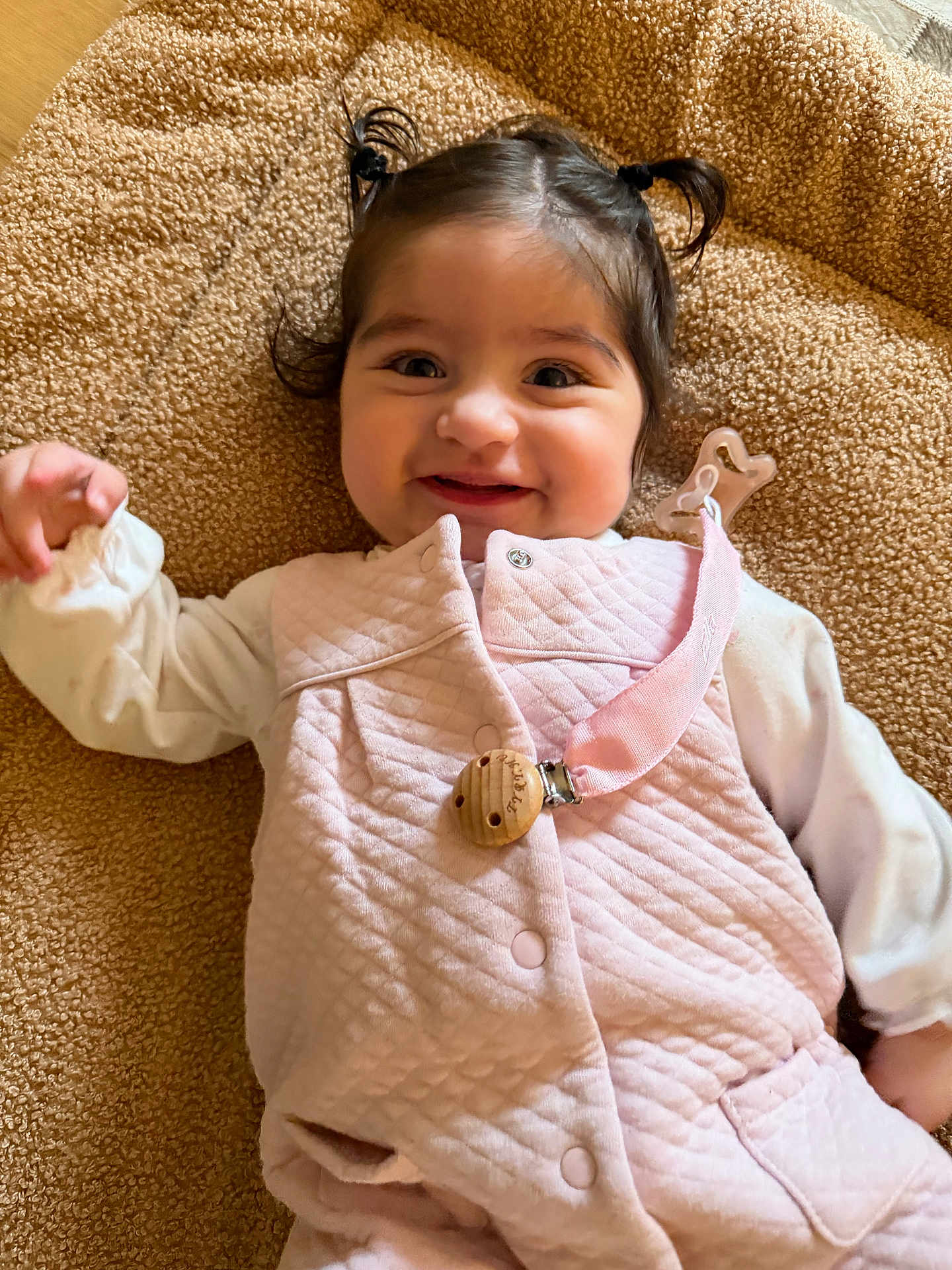 Ella participe au concours pour gagner de l'argent avec cette photo : baby, child, smile, happy, pigtails, pink_vest, blanket, lying_down, cute, indoor, portrait, person, infant, clothing, face, skin, hand, warm, soft, young